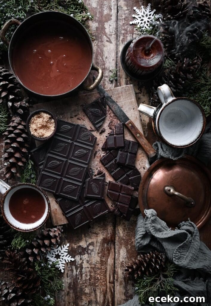 Chopped dark chocolate on cutting board next to pot of hot chocolate on table.