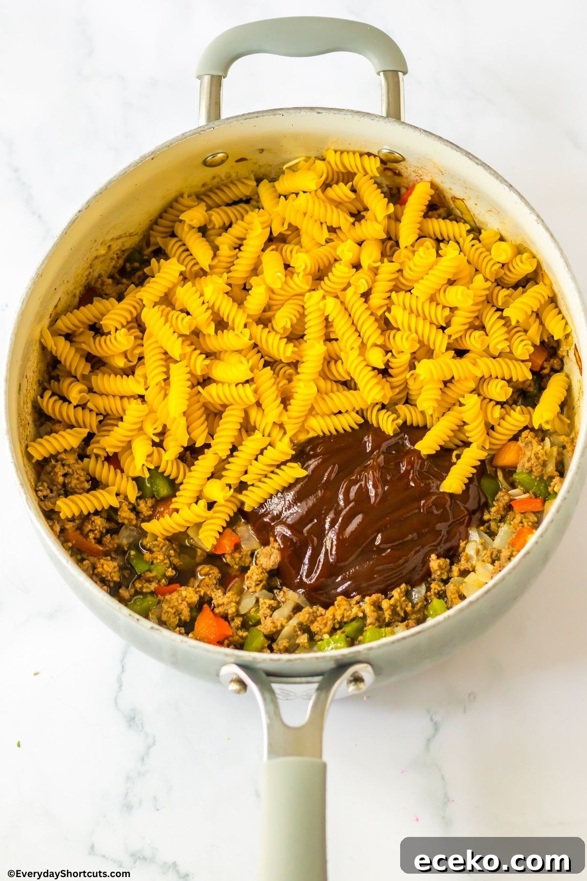 ground beef onions peppers bbq sauce and noodles in a pan