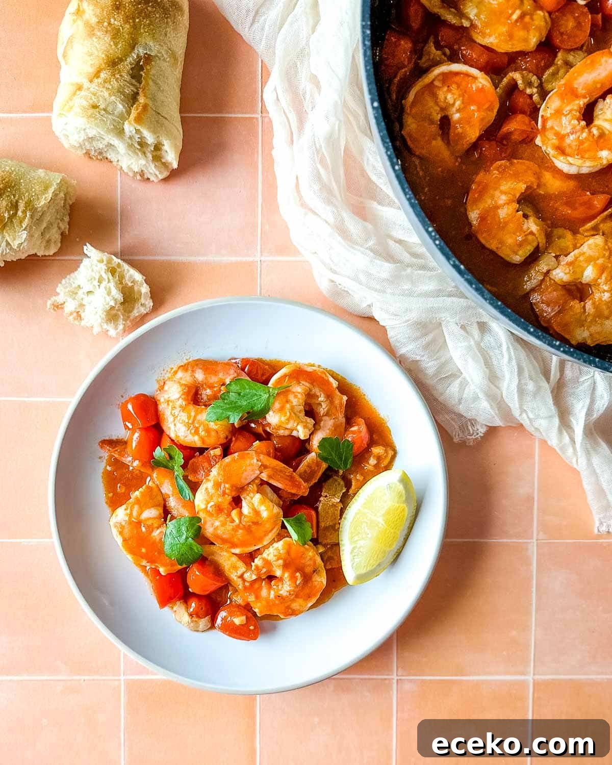 plate of bloody mary shrimp next to a pan of shrimp with a piece of baguette and a white linen.