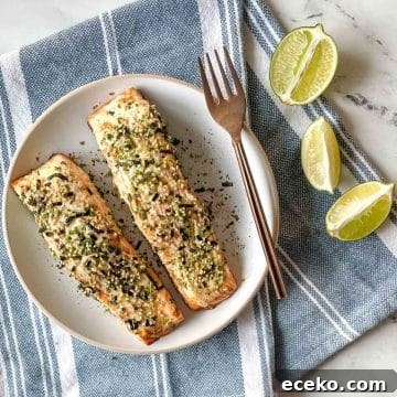 Two baked salmon fillets coated in mayonnaise and furikake sit on a white plate on a blue and white linen with lime slices.