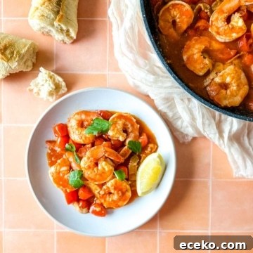 plate of bloody mary shrimp next to a pan of shrimp with a piece of baguette and a white linen.
