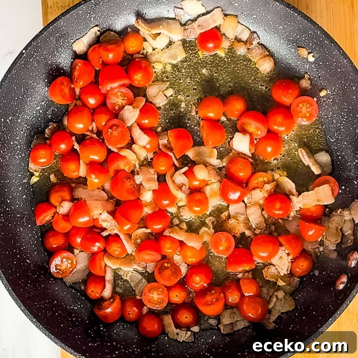 vodka, halved cherry tomatoes, bacon, and garlic cooking in pan.