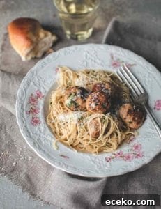 A patterned bowl filled with turkey meatballs with angel hair pasta, and a piece of bread and glass of white wine next to the bowl.