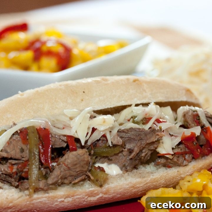 A hoagie roll on a red plate with shredded roast beef, onions, and bell peppers, with a white bowl of pickled peppers in the background.