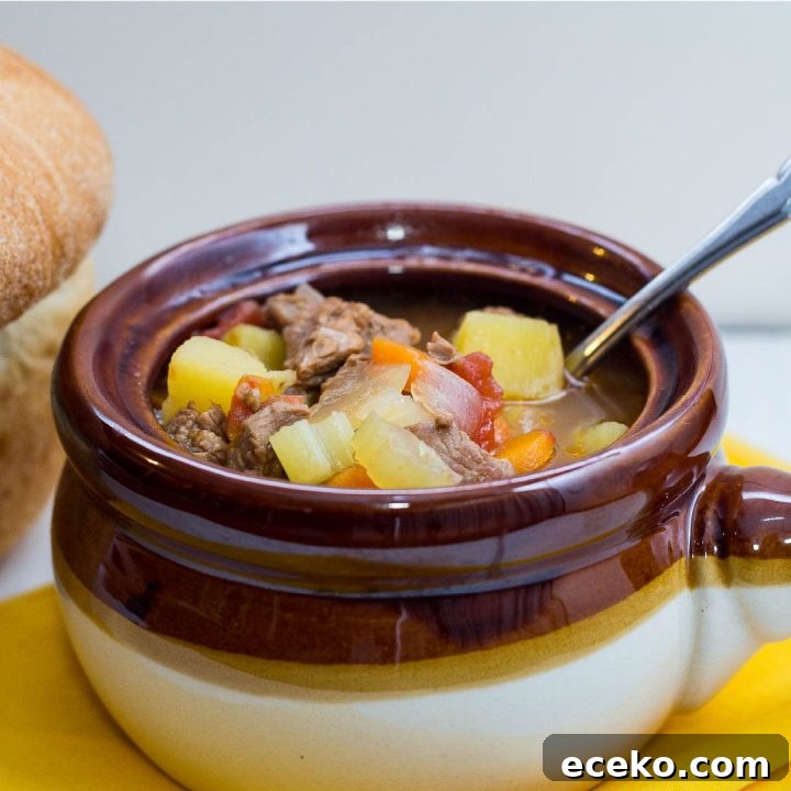 Brown and white soup bowl with vegetable beef soup and a spoon, next to a loaf of bread.