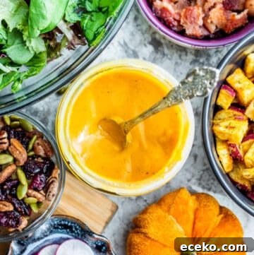 Overhead shot of pumpkin salad dressing in jar with silver spoon in it with salad ingredients.