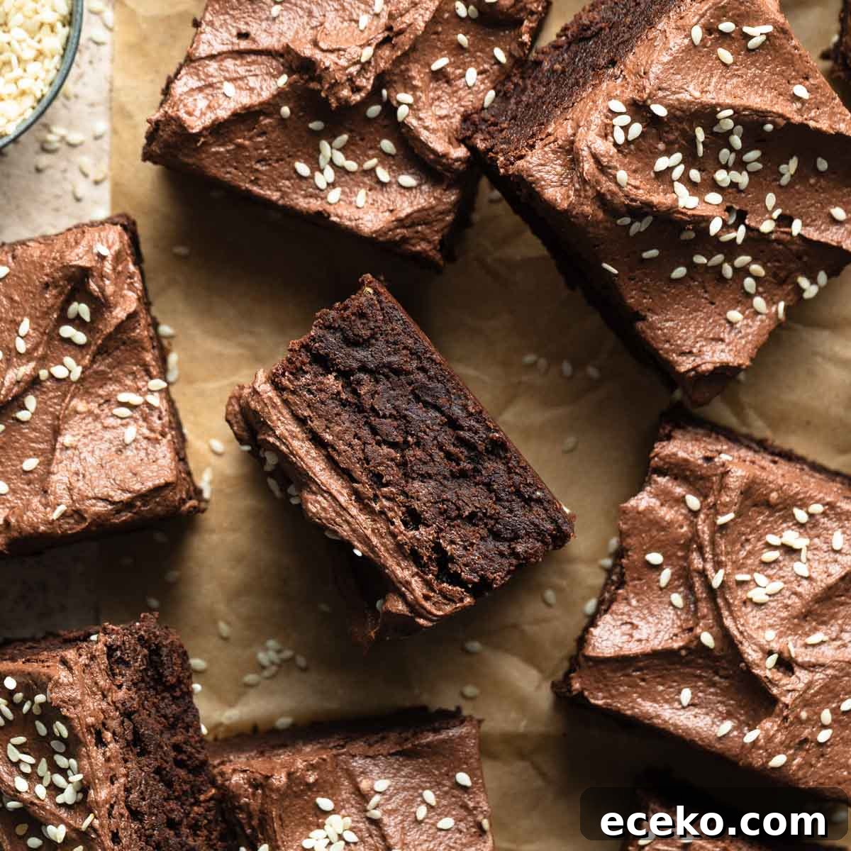 Frosted tahini brownies cut into squares and arranged on a sheet of brown parchment paper.
