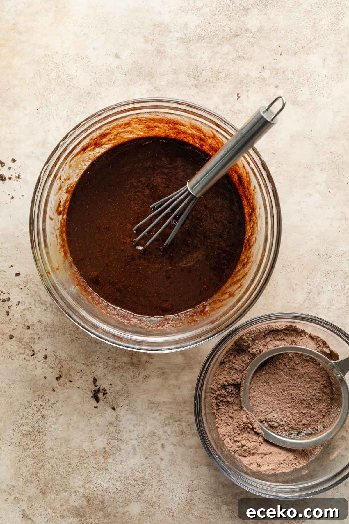 Wet chocolate mixture in a glass bowl next to a bowl of dry ingredients.