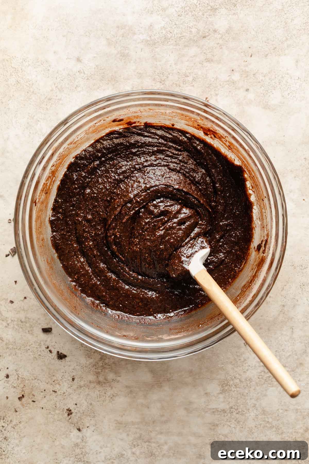 Brownie batter in a glass bowl with a spatula inserted into it.