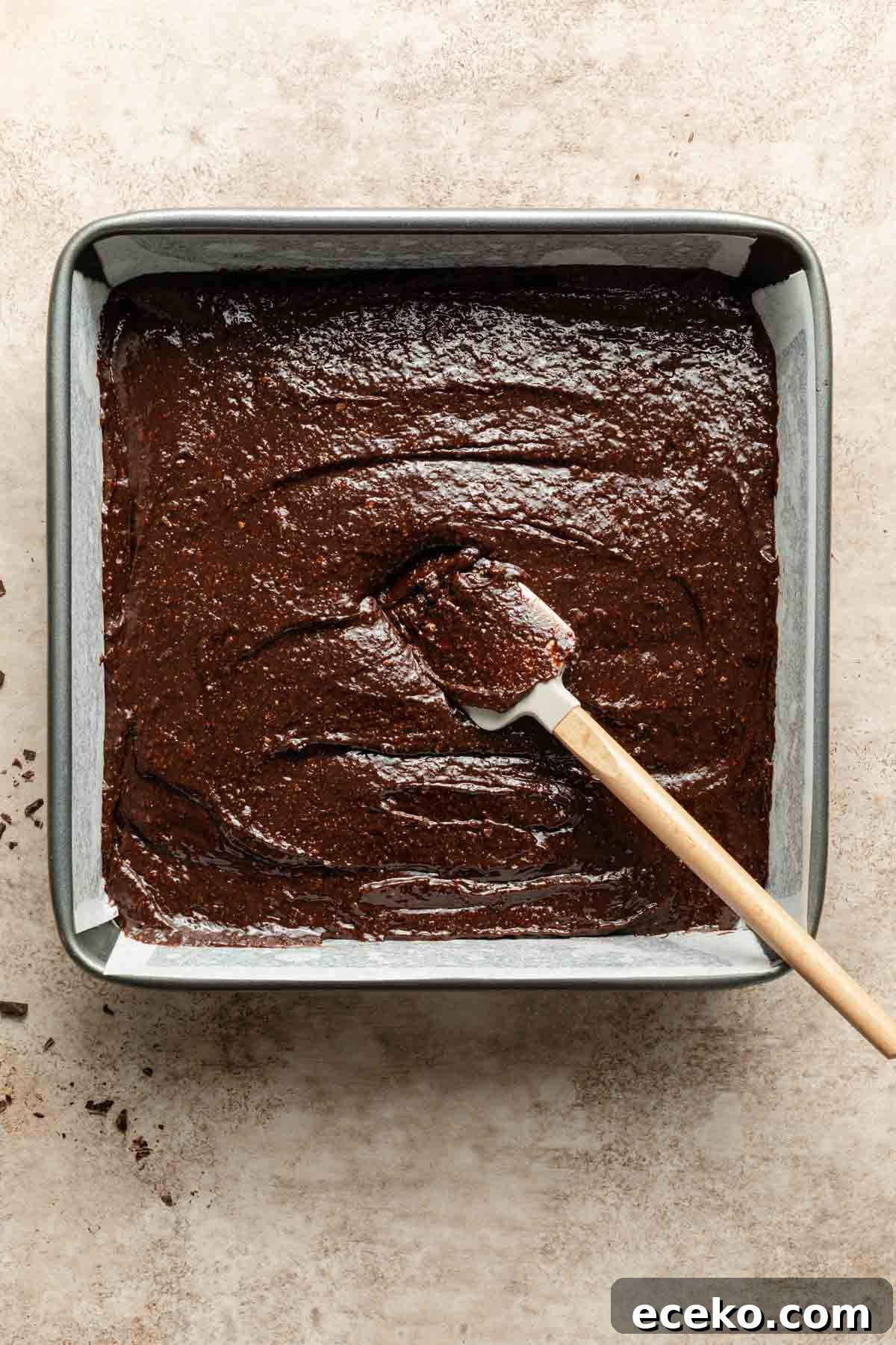 Brownie batter spread out in a square pan with a spatula.