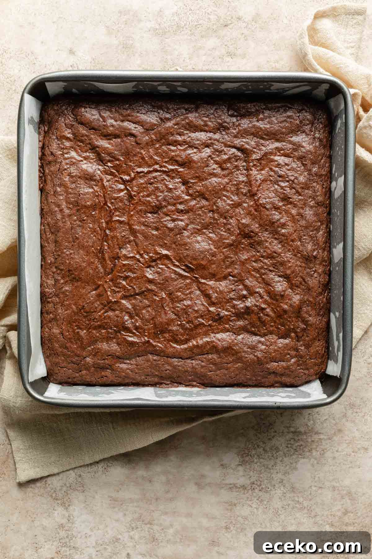 Brownies baked up in a square pan and resting on a beige cloth.
