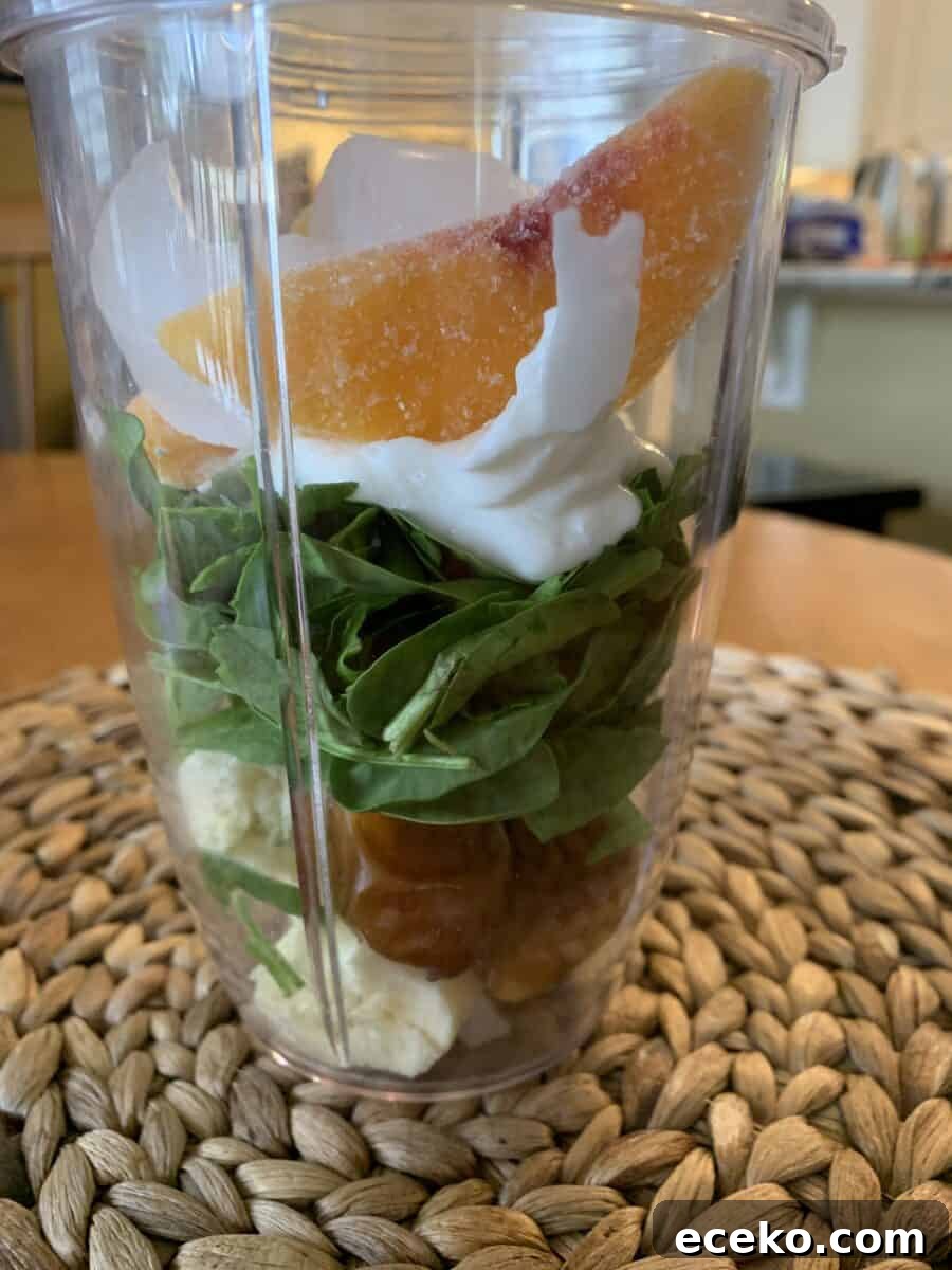 Peach slices on top of smoothie ingredients in a blender cup 