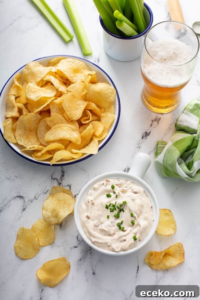 Creamy Homemade French Onion Dip Recipe for Parties 3 Overhead view of a bowl of french onion dip on a counter next to a bowl of potato chips and a glass of beer