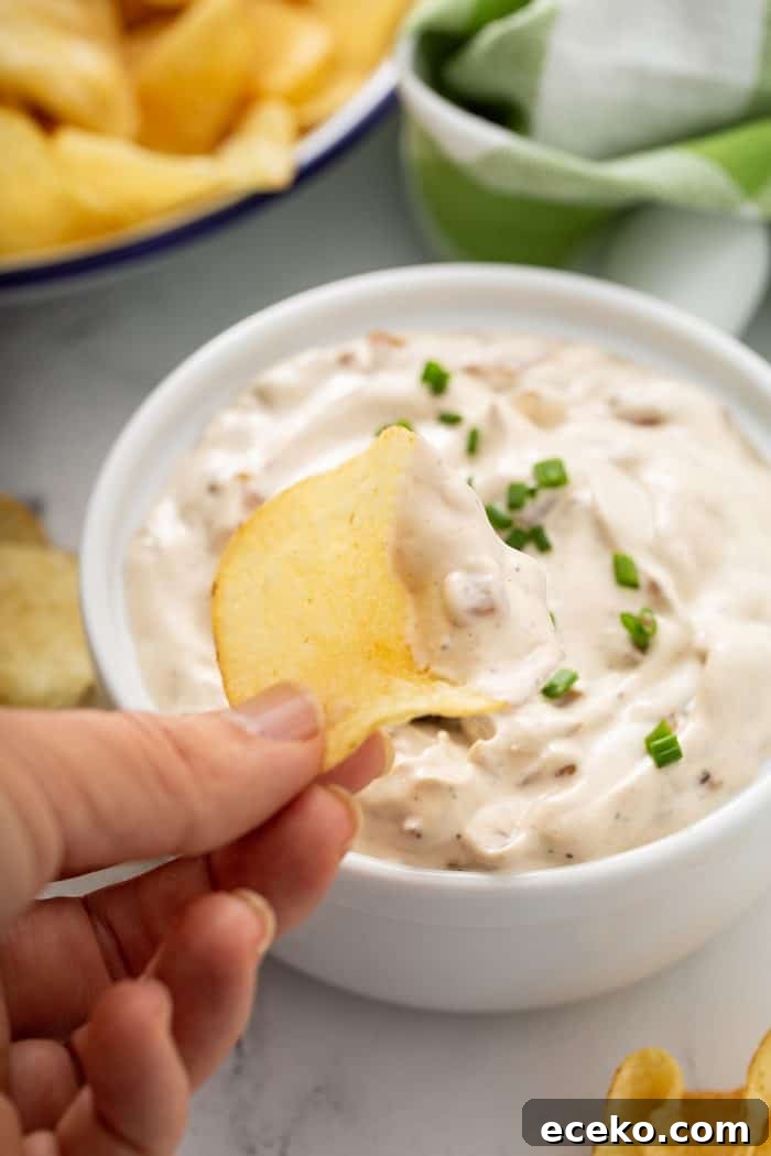 Creamy Homemade French Onion Dip Recipe for Parties 10 Hand scooping up french onion dip with a potato chip