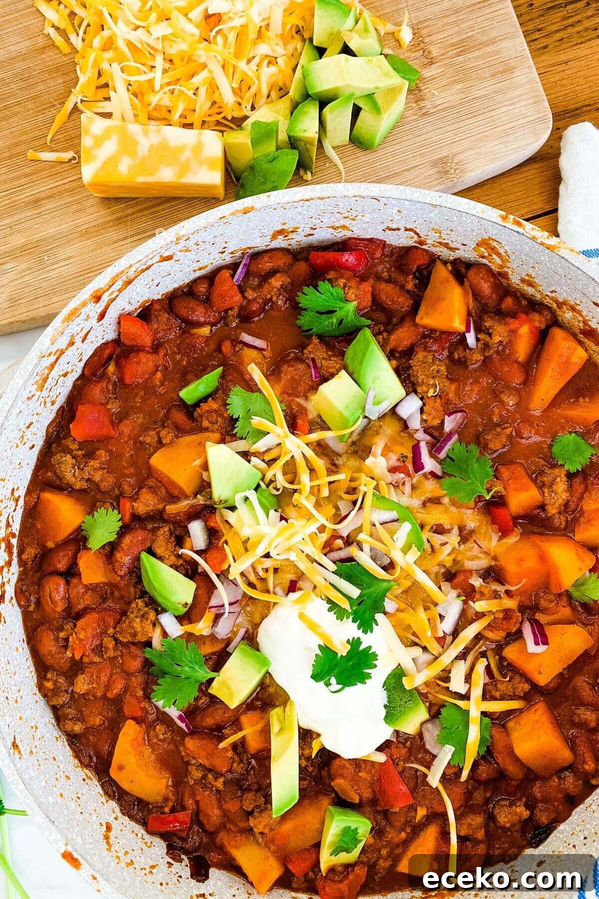 Beef and butternut squash chili in a pot topped with avocado, cheese and sour cream.