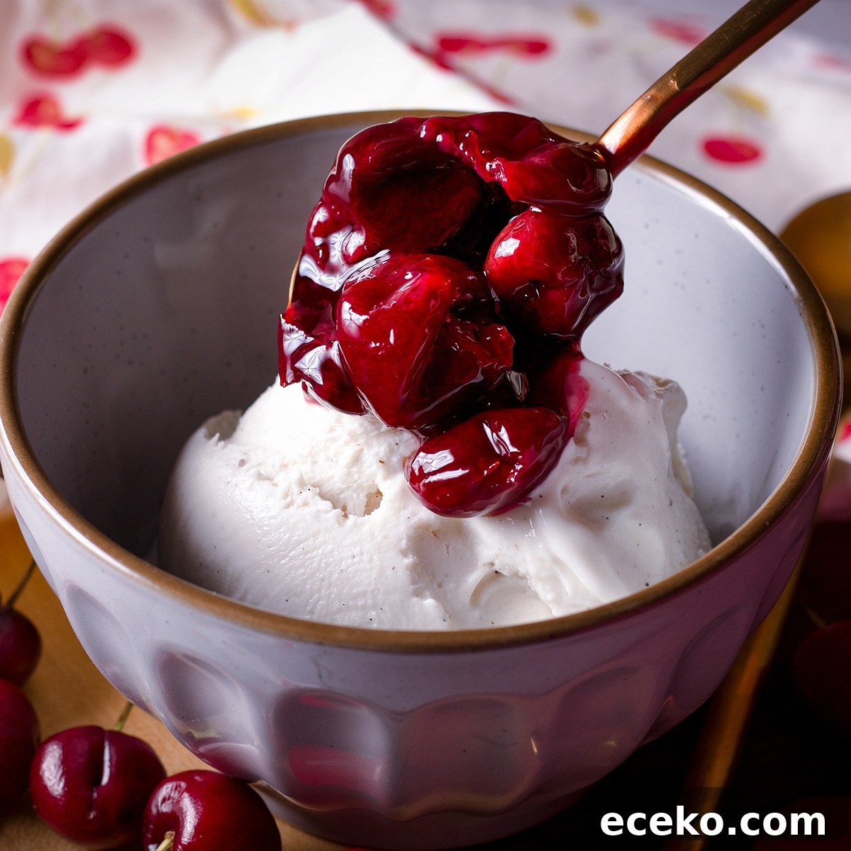 Spooning cherry sauce over a bowl of vanilla ice cream.