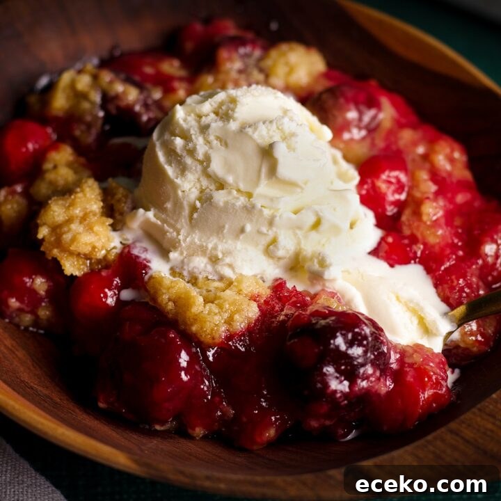 A bowl of cherry cobbler topped with a scoop of vanilla ice cream.