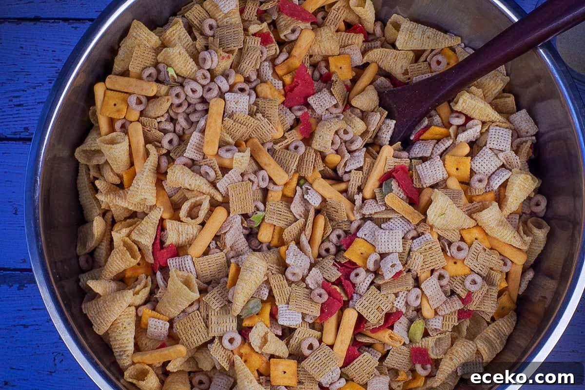 Cheerios, Life cereal, Chex cereal, pretzels (missing in photo), Bugles, pistachios, cheese nips, cheese bits, and red tortilla chips mixed together in large stainless steel bowl.