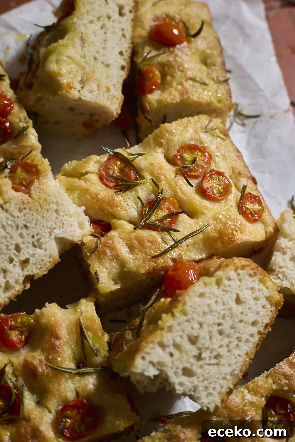 Slices of focaccia topped with cherry tomatoes on white parchment paper.