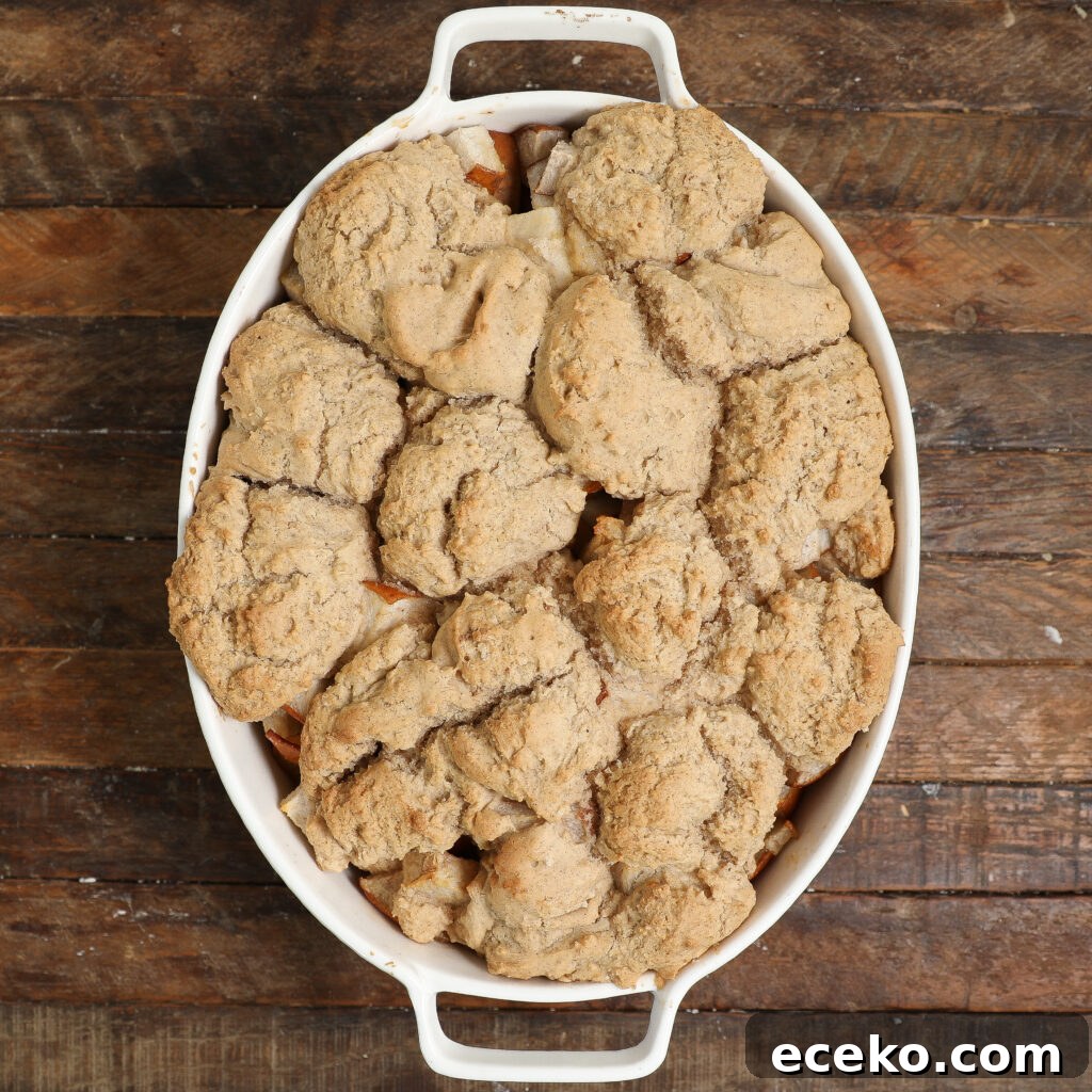 Warm Pear Cobbler with Cinnamon and Brown Sugar 4 A white oval baking dish filled with a golden-brown pear cobbler, featuring a biscuit-like topping, sits on a rustic wooden surface.