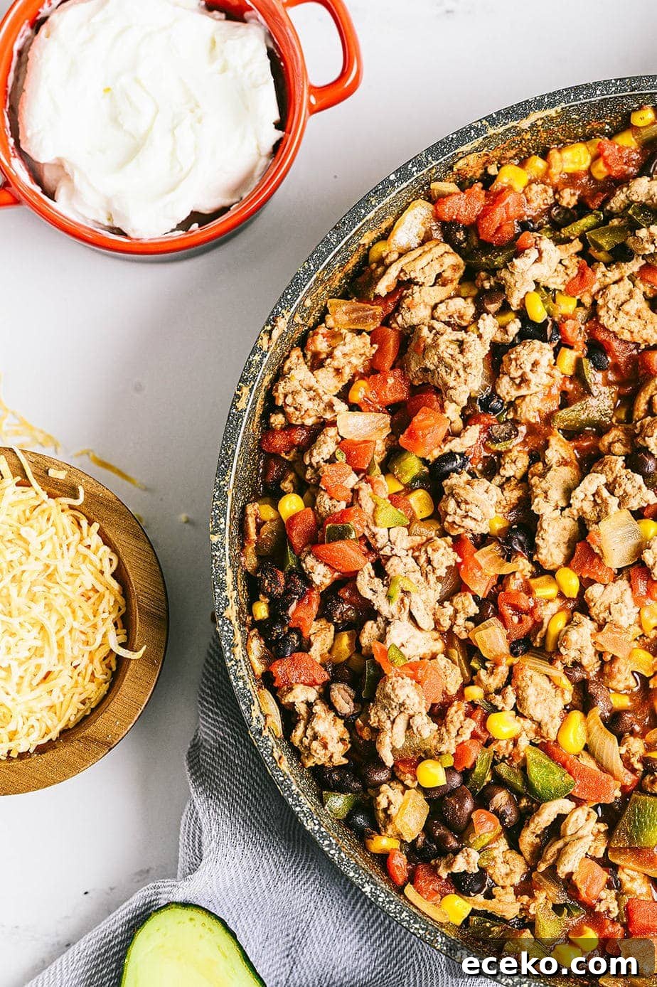 One-Skillet Taco Skallowder: Quick Mexican-Style Skillet Dinner 2 An overhead shot of a skillet with ground turkey, bell peppers, beans, corn, and onions. Yogurt, cheese, and avocado sit nearby as toppings