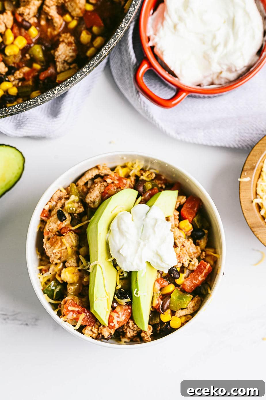 One-Skillet Taco Skallowder: Quick Mexican-Style Skillet Dinner 5 A white marble background with a small bowl of taco skillet topped with avocado and greek yogurt. The remaining skillet sits nearby, as well as a bowl of plain greek yogurt.