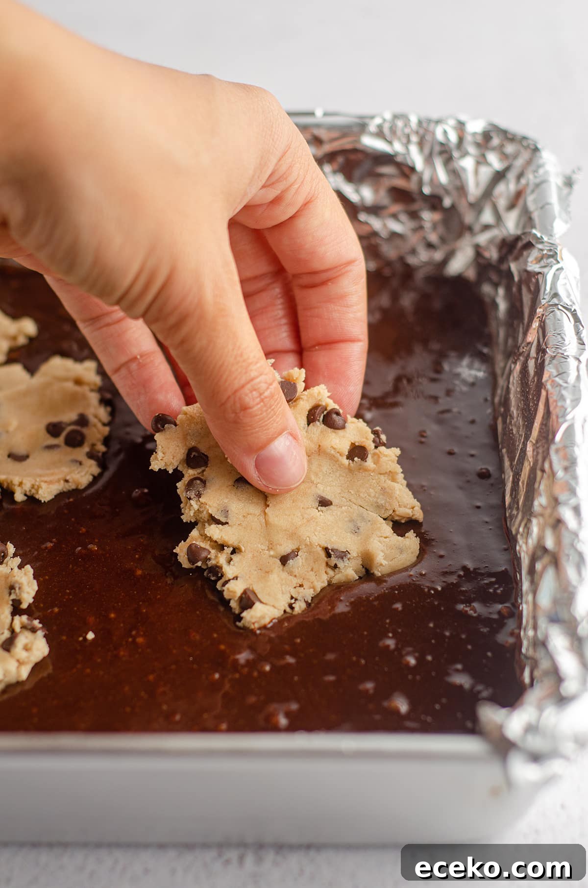 Cookie Dough Stuffed Brownies: Decadent Chocolate Dessert Recipe 12 a hand layering cookie dough pieces onto brownie batter