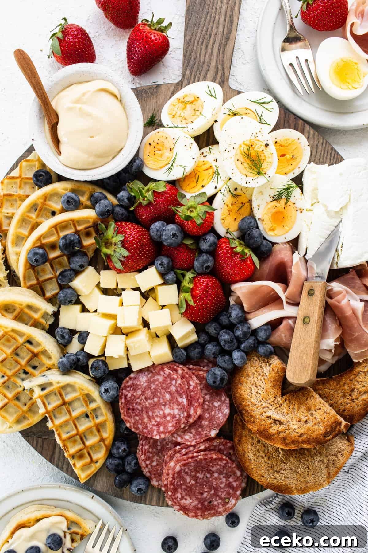 A platter with a variety of meats, cheeses, fruits and waffles.