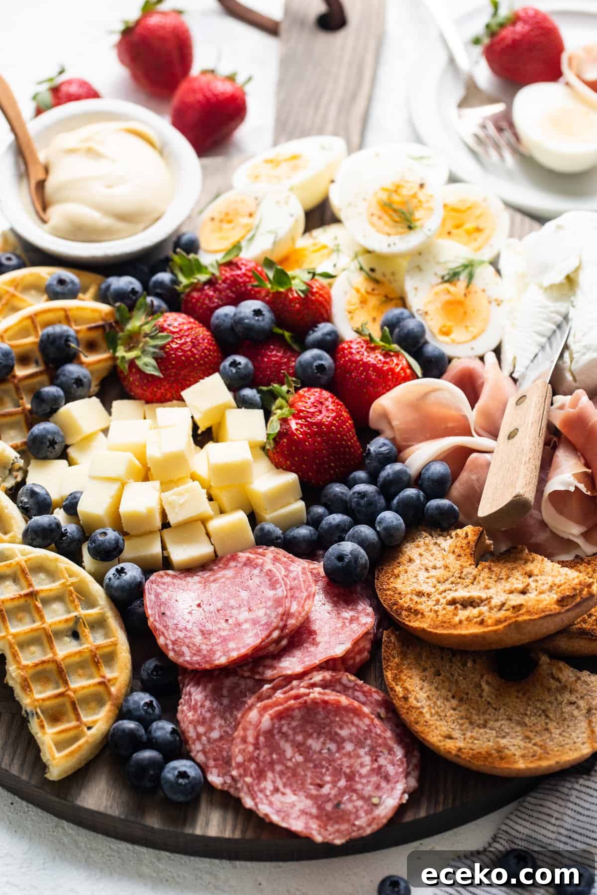 A platter with a variety of meats, cheeses, fruits and waffles.