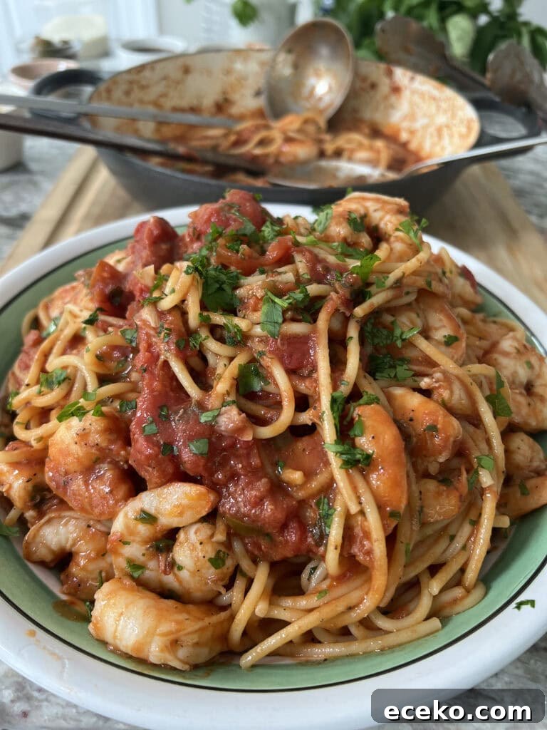 Spicy Shrimp Arrabbiata Pasta with Garlic Tomato Sauce 3 Pasta bowl filled with spicy shrimp marinara with parsley garnish and pan in background with spoon.