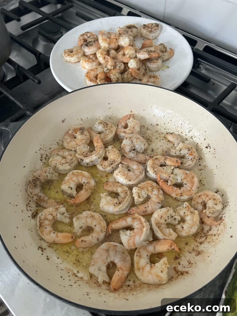Spicy Shrimp Arrabbiata Pasta with Garlic Tomato Sauce 7 Searing shrimp on olive oil in pan with plateful of cooked shrimp in background.