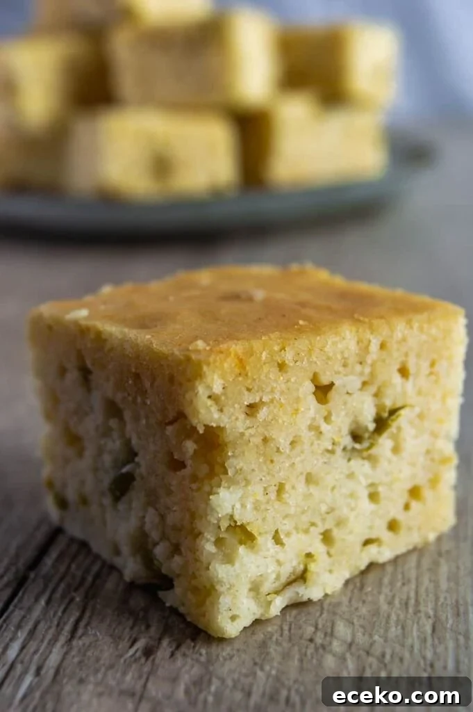 Spicy Vegan Jalapeño Cornbread Recipe 8 Close up of a cube of cornbread on wood with a plate in the background