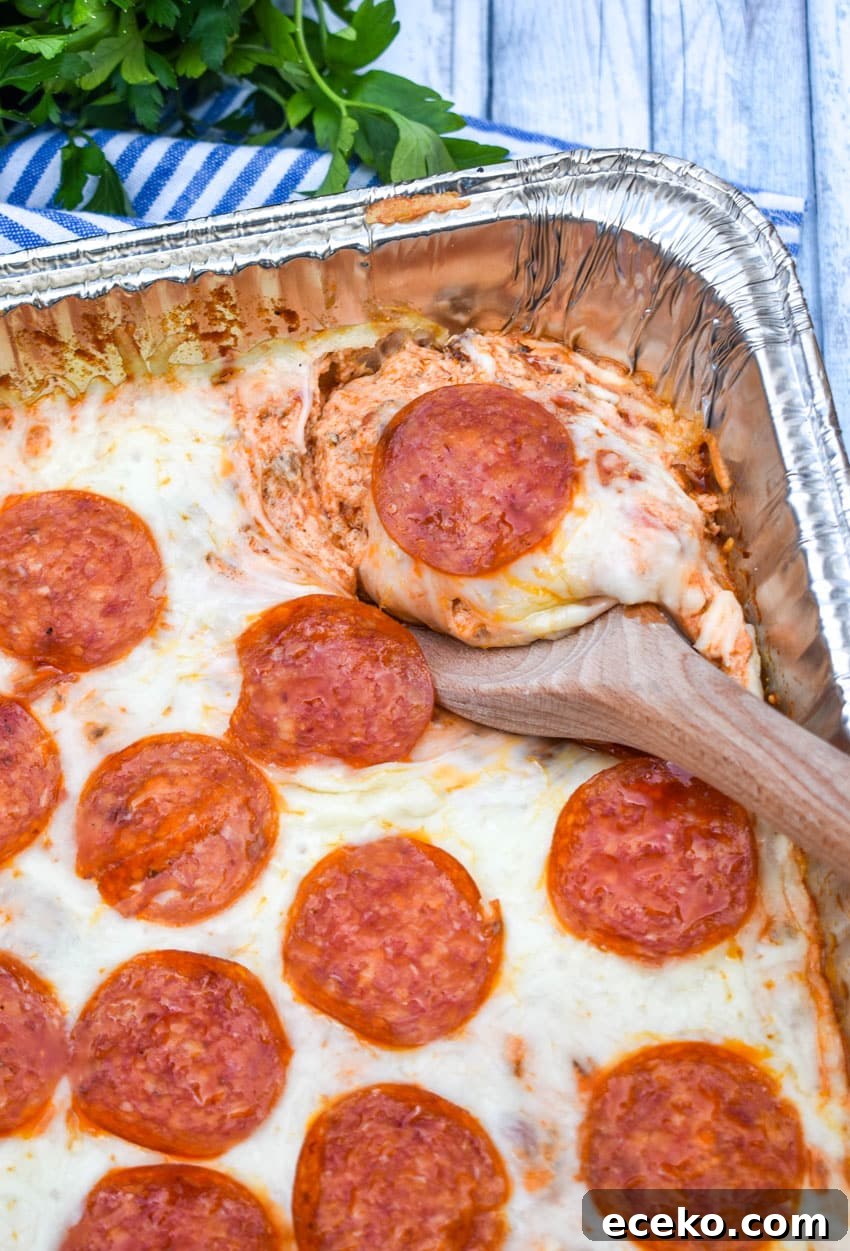 a wooden spoon scooping smoked pepperoni pizza dip out an aluminum pan