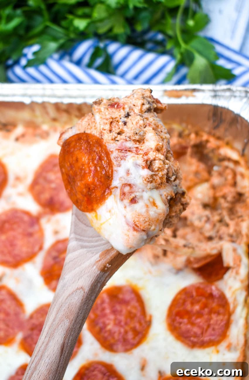 a wooden spoon holding up a scoop of smoked pepperoni pizza dip
