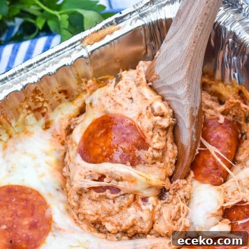 a wooden spoon scooping smoked pepperoni pizza dip out an aluminum pan