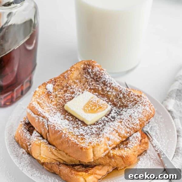 French toast stacked on a plate with powdered sugar, butter, and maple syrup.