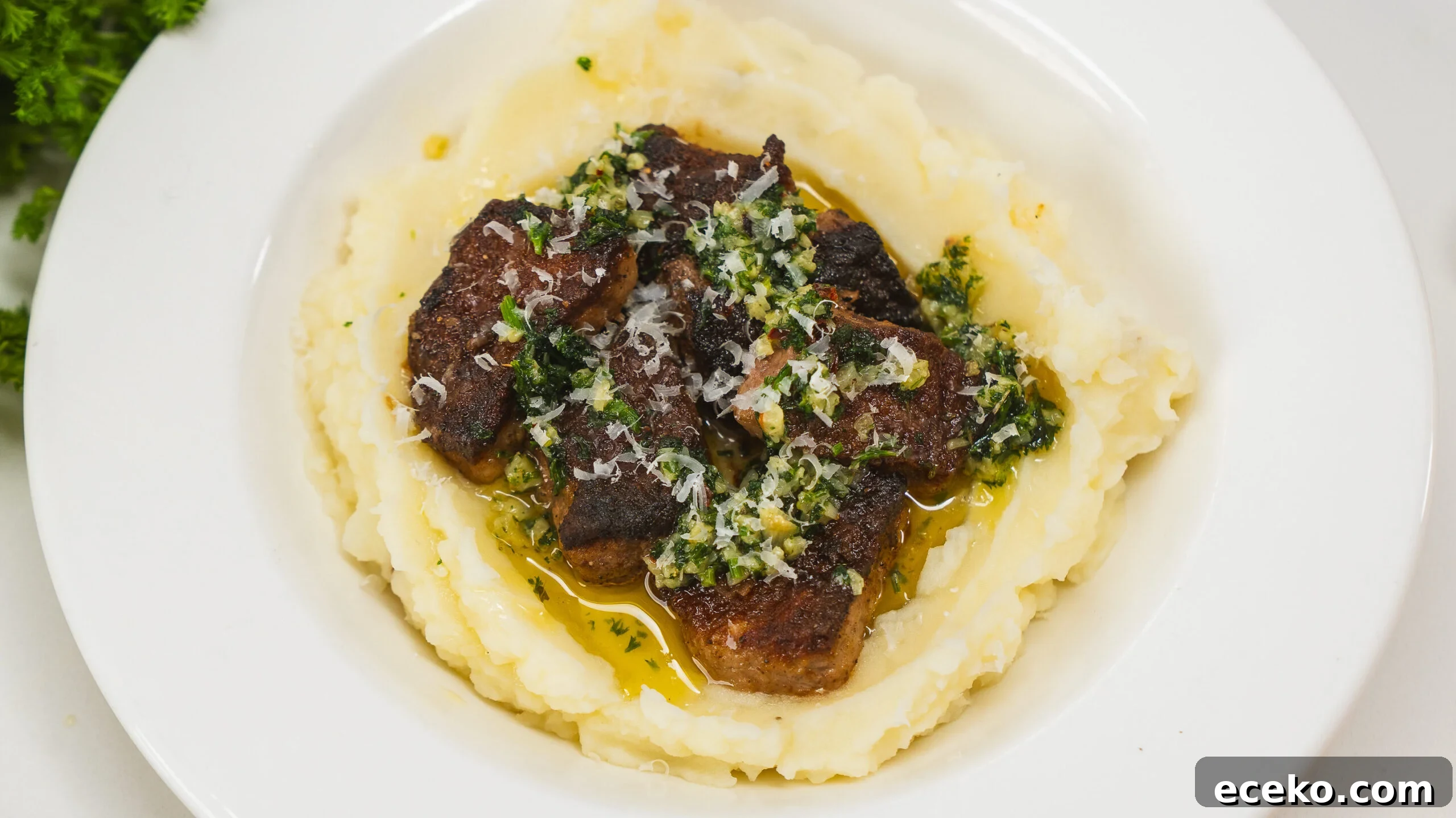 Garlic butter steak bites served over mashed potatoes in a white bowl.