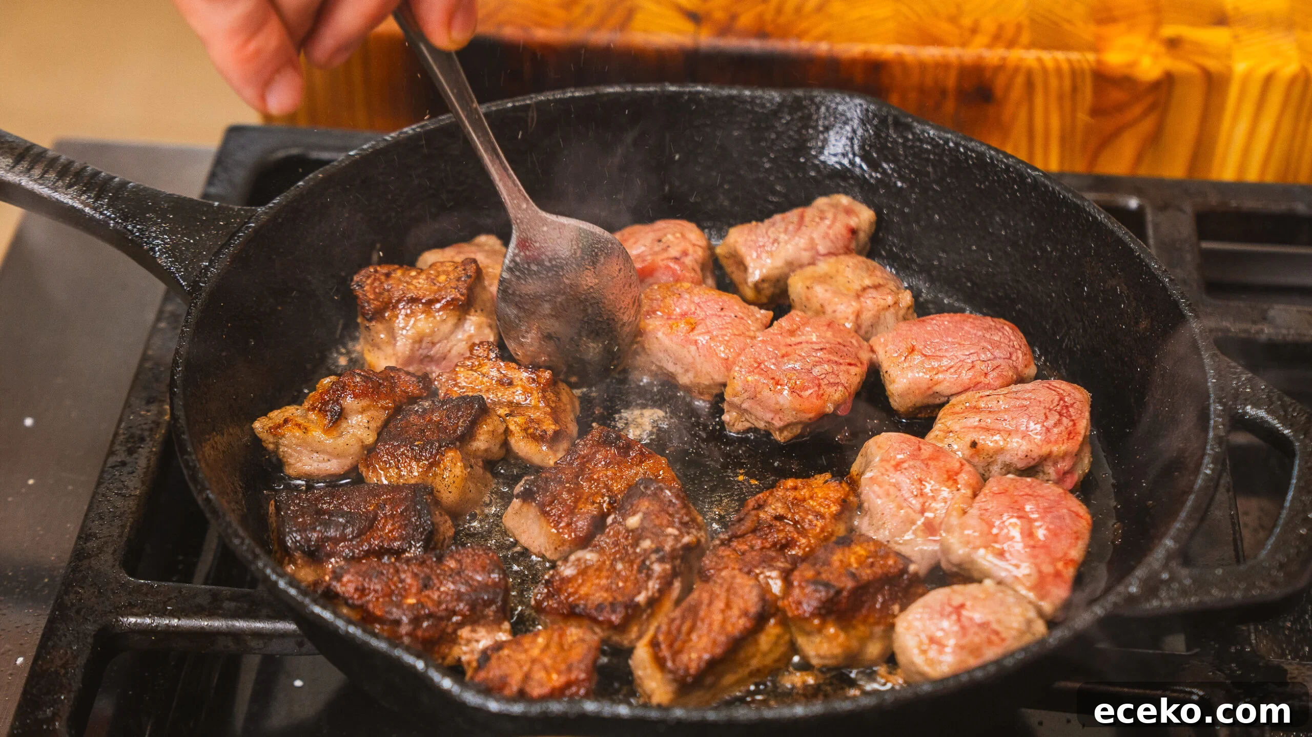 Steak bites being seared in a. cast iron pan.