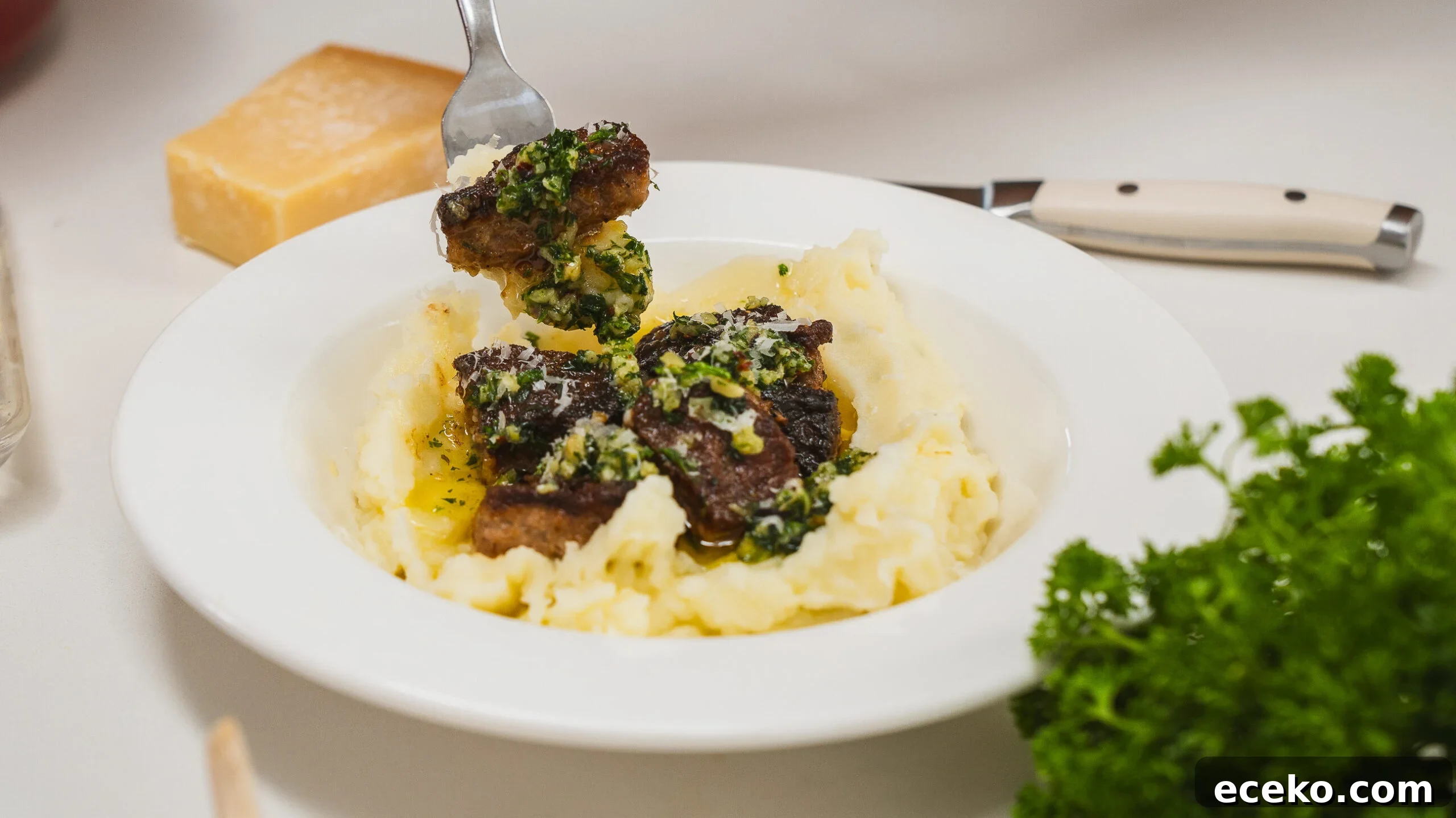Garlic. butter steak bites in a white bowl served over mashed potatoes.