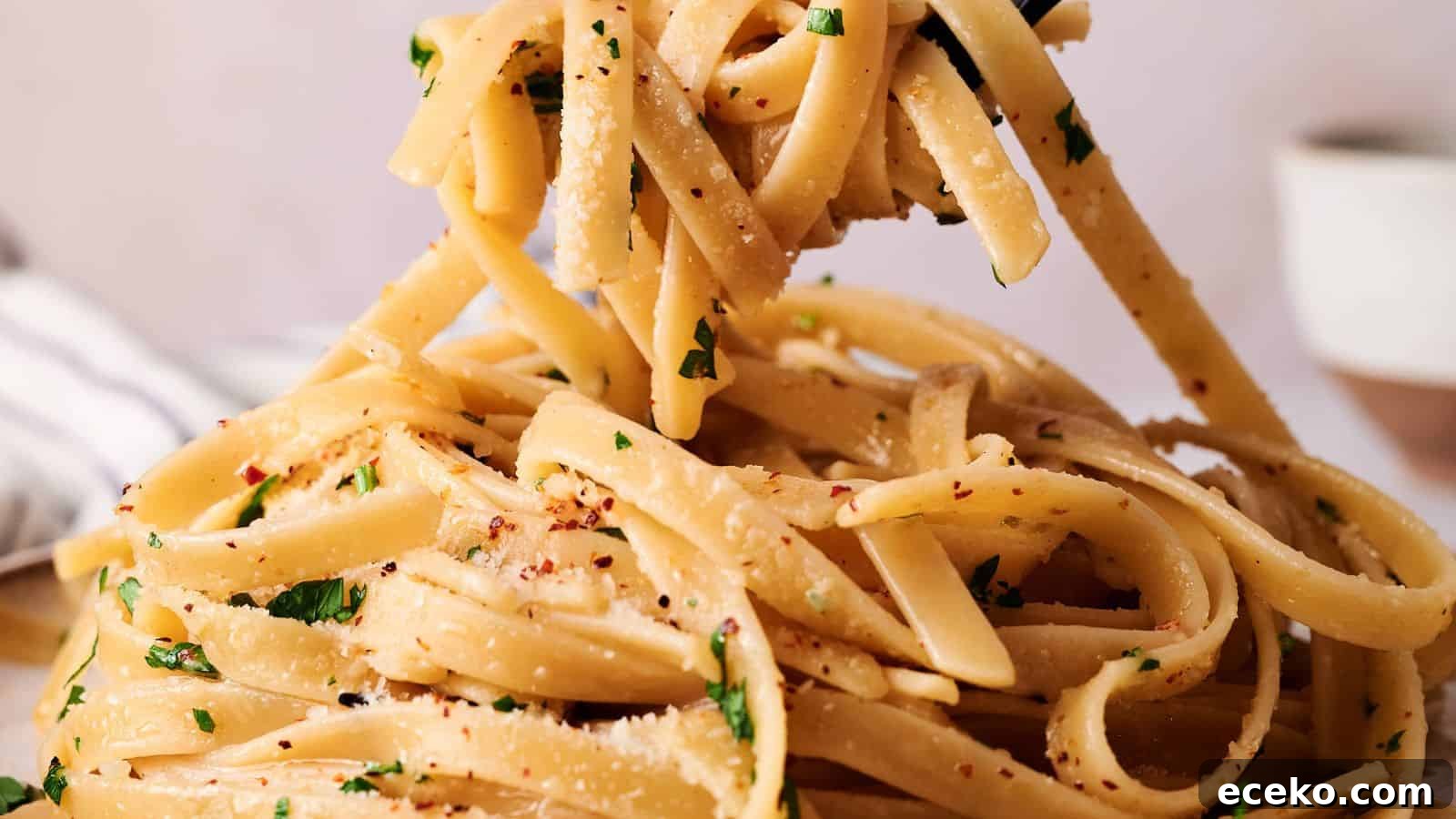 Close-up of fettuccine pasta tossed with grated cheese, chopped parsley, and red pepper flakes being lifted with a fork.