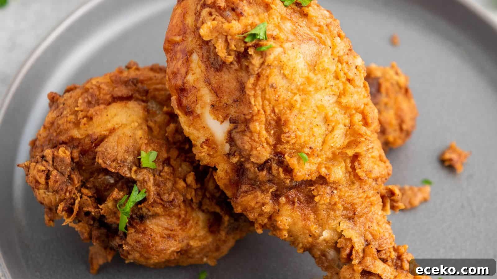 Two pieces of fried chicken on a gray plate, garnished with small bits of green herbs.