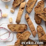 Vegan gingerbread biscotti on a white surface with a bowl of candied ginger and some ribbons.