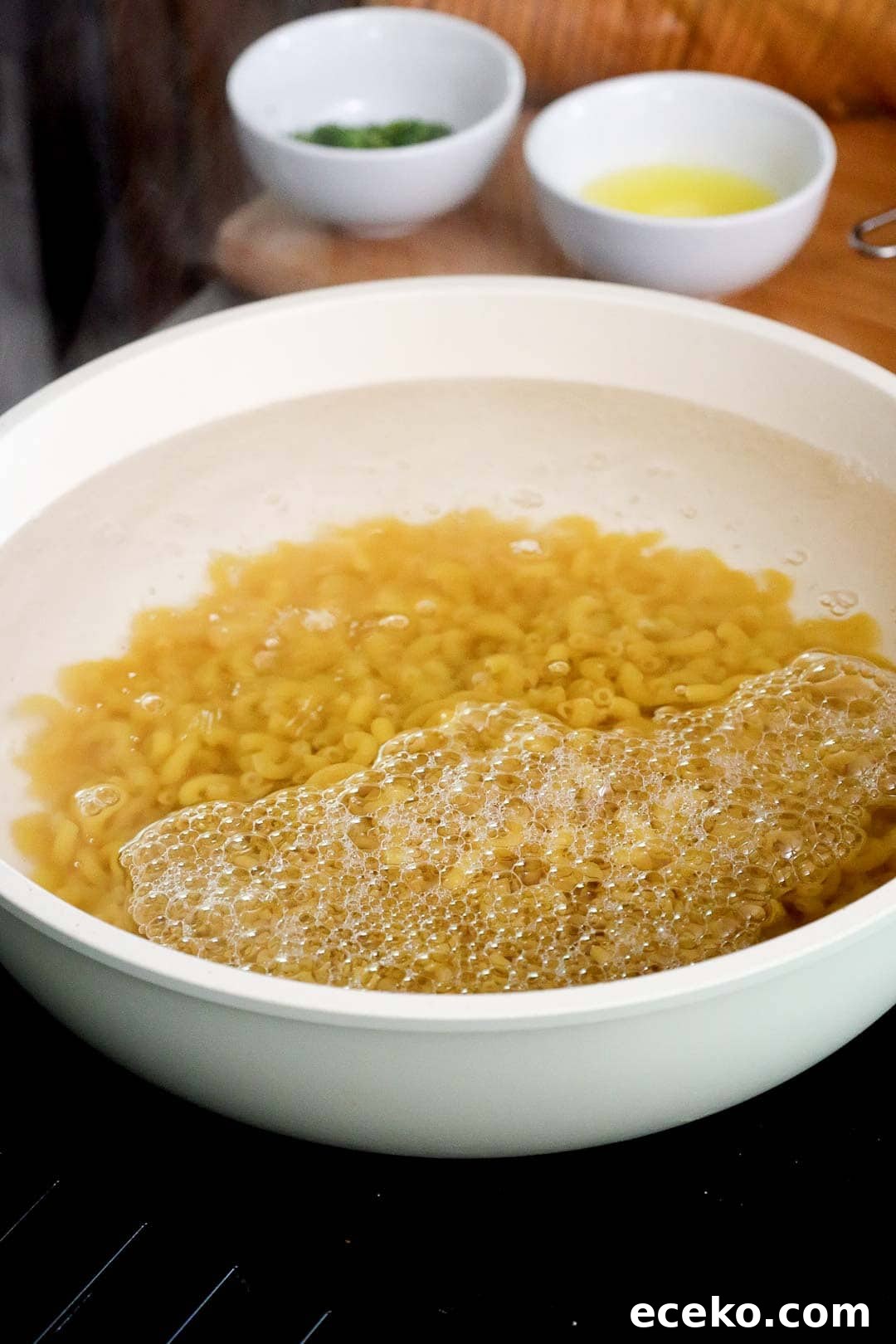 Elbow macaroni boiling in a large white pot of bubbling water.