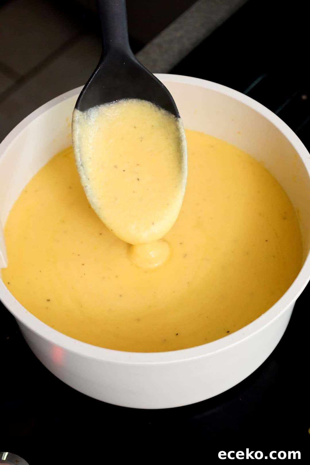 Thick, creamy cheese sauce made from shredded cheddar and milk being stirred with a spoon in a saucepan.