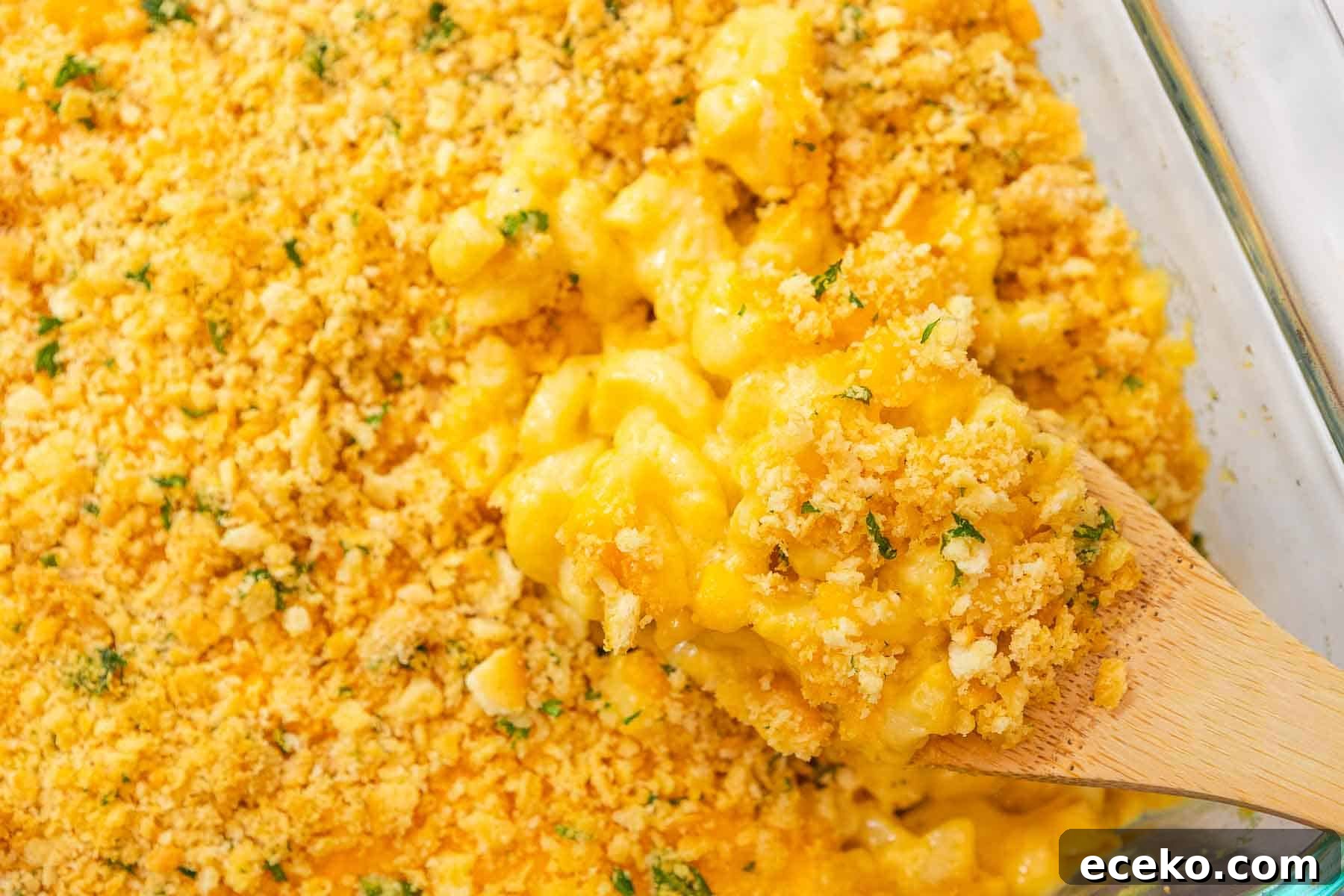 Wooden spoon scooping creamy cheddar mac and cheese topped with crumbled cracker topping out of a casserole dish.