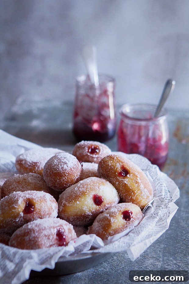 How to Make Homemade Jelly-Filled Doughnuts from Scratch 2 Homemade yeast doughnuts filled with raspberry jam in a bowl next to a jar of raspberry jam.