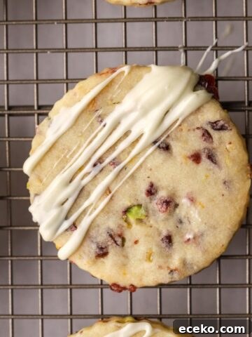 Cranberry shortbread cookies on a rack drizzled with white chocolate.