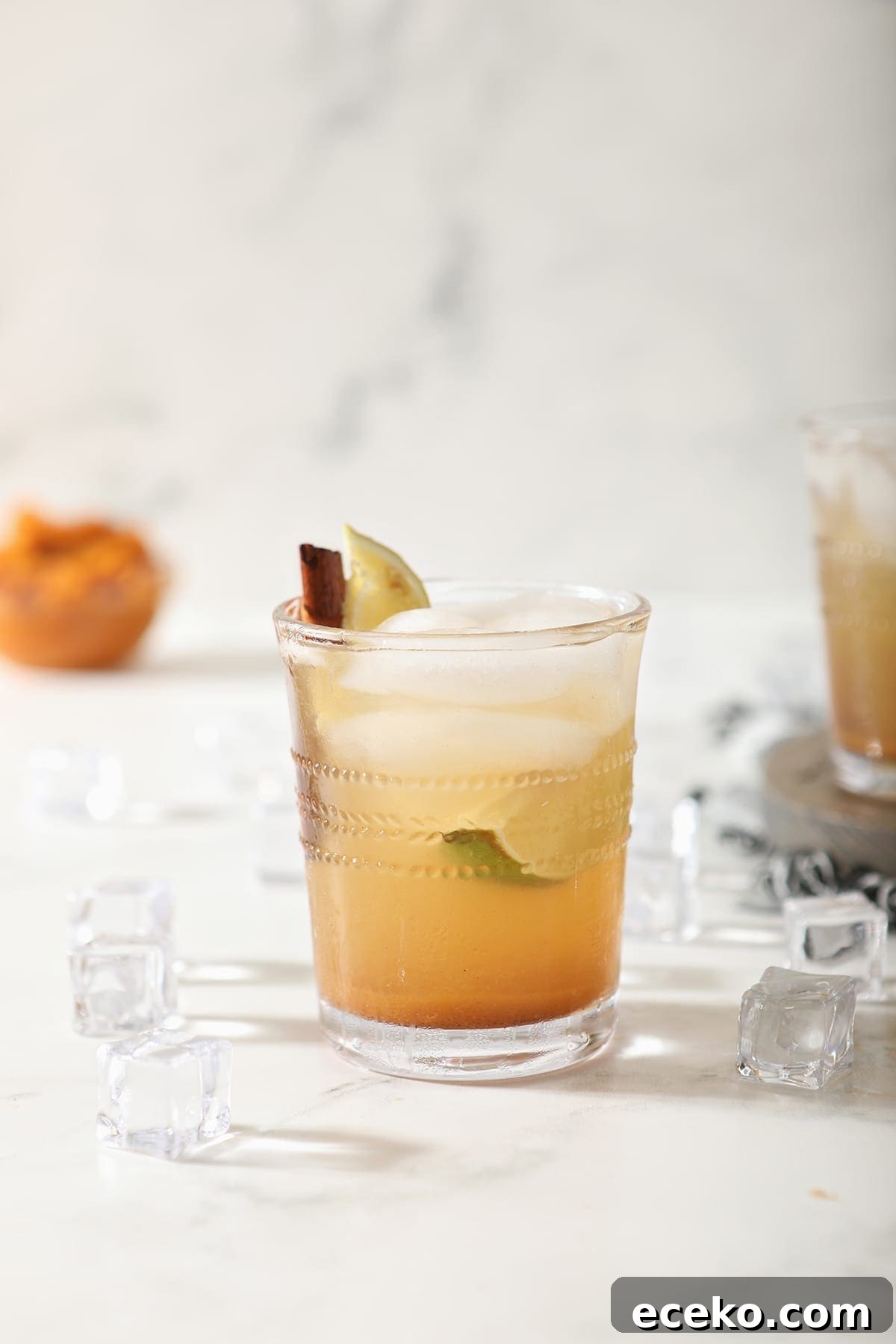 A singular glass of Pumpkin Spice Mule on marble with a bowl of pumpkin puree behind it
