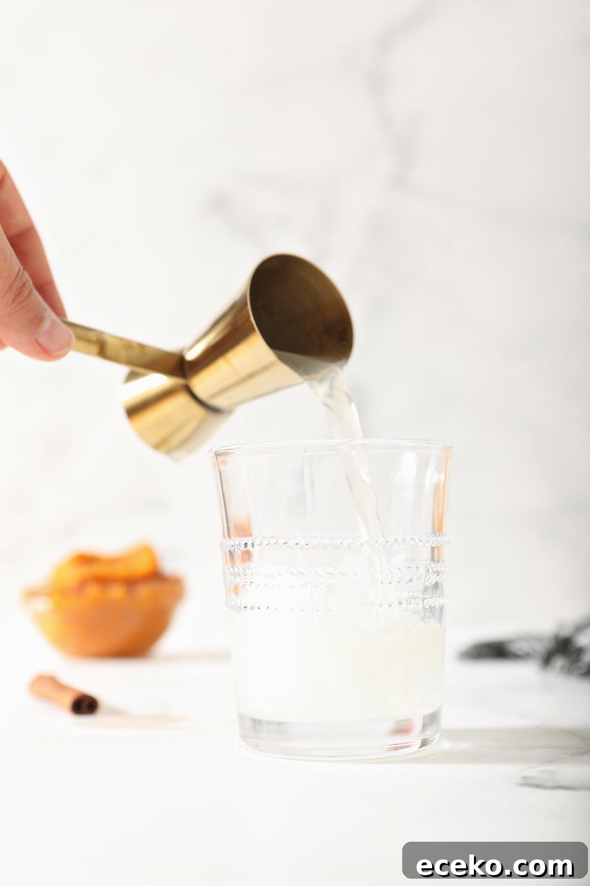 Ginger beer pours into a glass from a gold jigger