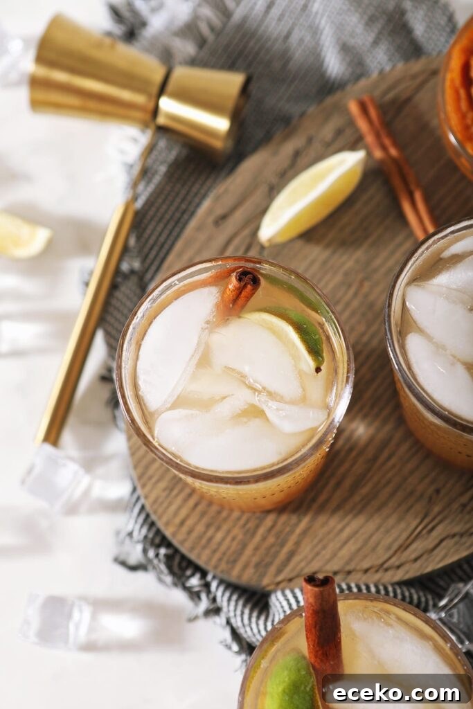 Overhead of three Pumpkin Spice Moscow Mules on a wooden serving dish next to to limes, a jigger and a bowl of pumpkin puree